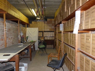 The crypt in St Bride's, London, where radiological examination took place. The stacked and labeled cardboard boxes contain the bones of an individual recovered from each lead coffin. The table on the left of the image was used for taking x-rays with a portable unit.
