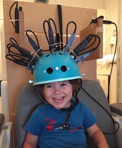 A child undergoing imaging with the MEG helmet scanner. Image courtesy of Dr. Rebeccah Slater from the University of Oxford.