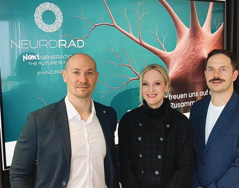 Three professionals posing at NeuroRad Next Generation conference event with turquoise branded backdrop featuring neural imagery
