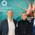 Three professionals posing at NeuroRad Next Generation conference event with turquoise branded backdrop featuring neural imagery