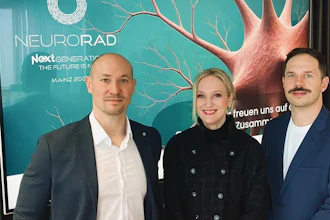 Three professionals posing at NeuroRad Next Generation conference event with turquoise branded backdrop featuring neural imagery