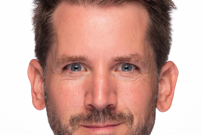 Professional headshot of a man with dark hair and facial hair against a white background