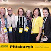 Six women smile together at ASHNR Pittsburgh Homecoming event celebrating 60 years of Head & Neck Radiology, all wearing credential badges