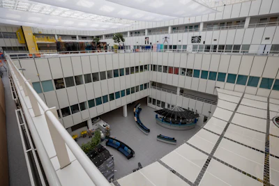 Modern multi-story building atrium with white paneled walls, skylights, and people gathered in the courtyard below