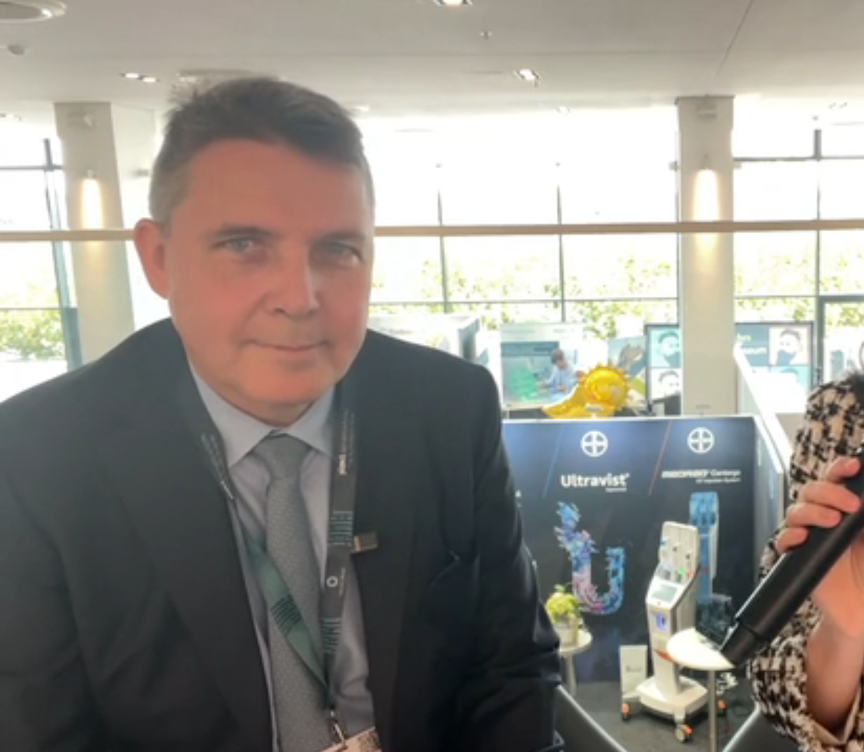 Professional man in dark suit at medical conference with Ultravist product display in background