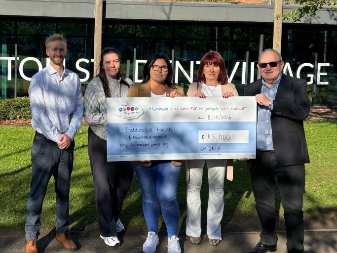 Five people holding a large ceremonial check for £45,000 charity donation in front of Town Centre Village storefront