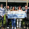 Five people holding a large ceremonial check for £45,000 charity donation in front of Town Centre Village storefront