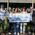 Five people holding a large ceremonial check for £45,000 charity donation in front of Town Centre Village storefront