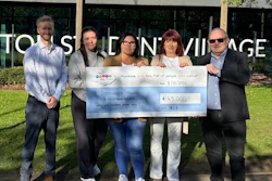 Five people holding a large ceremonial check for £45,000 charity donation in front of Town Centre Village storefront