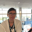 Professional woman wearing glasses and beige cardigan at indoor conference venue with modern architecture and blue displays
