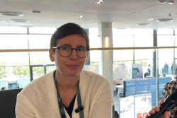 Professional woman wearing glasses and beige cardigan at indoor conference venue with modern architecture and blue displays