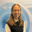 Smiling woman with glasses wearing professional black and white attire in front of futuristic blue circular design
