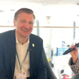 Professional man in navy blazer smiling at conference event wearing ID badge
