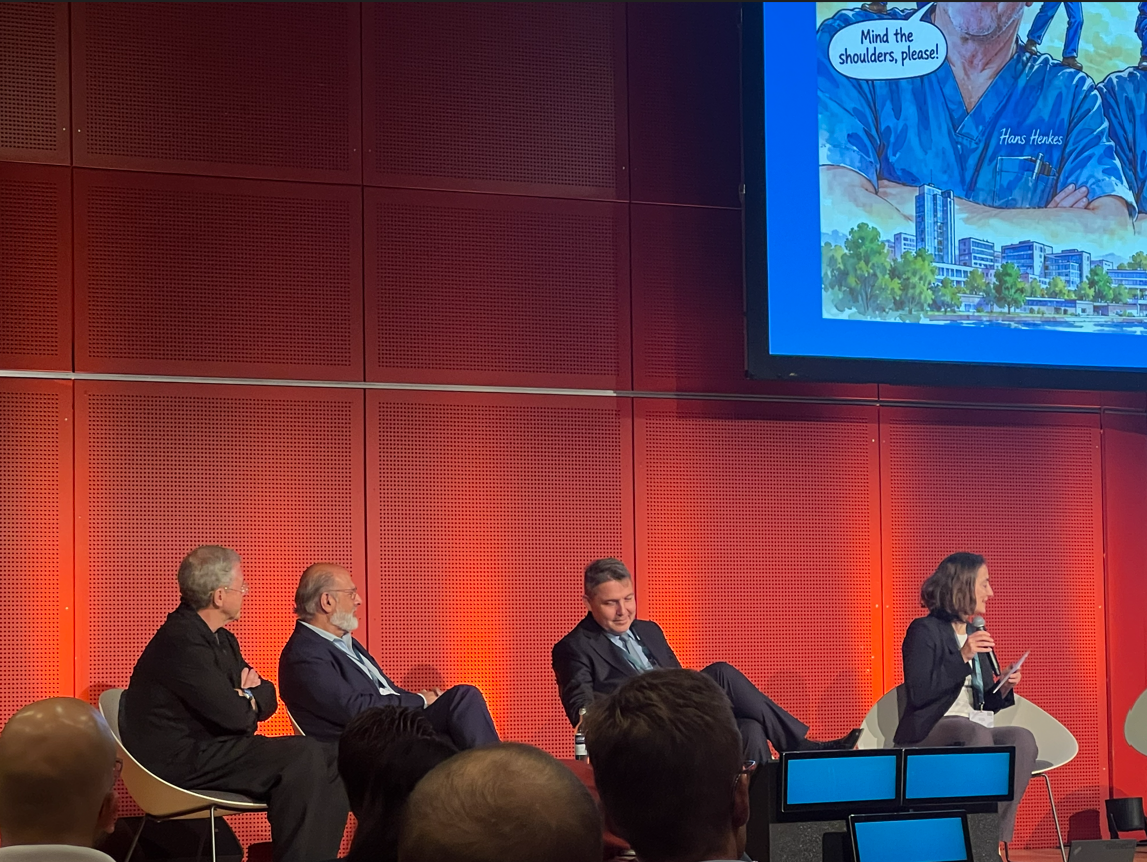 Panel discussion with four business professionals seated on stage against red LED backdrop at conference event