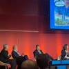 Panel discussion with four business professionals seated on stage against red LED backdrop at conference event