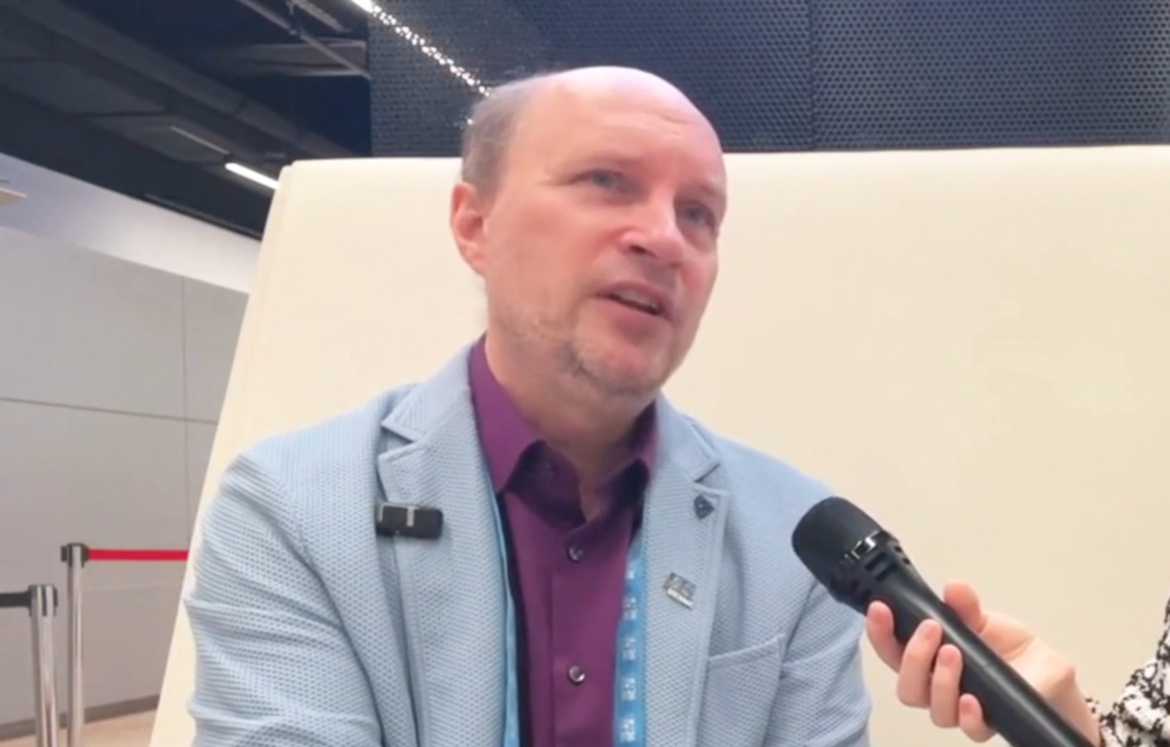 Professional man in light blue blazer speaking at conference with microphone and lanyard badge