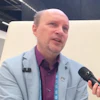 Professional man in light blue blazer speaking at conference with microphone and lanyard badge