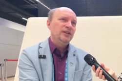 Professional man in light blue blazer speaking at conference with microphone and lanyard badge