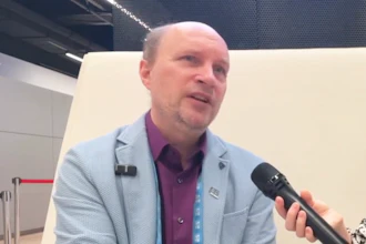 Professional man in light blue blazer speaking at conference with microphone and lanyard badge