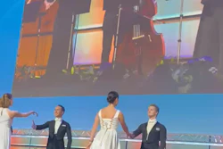 Formal event on stage with elegantly dressed guests and musicians performing on large screen display above