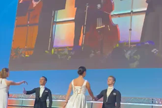 Formal event on stage with elegantly dressed guests and musicians performing on large screen display above