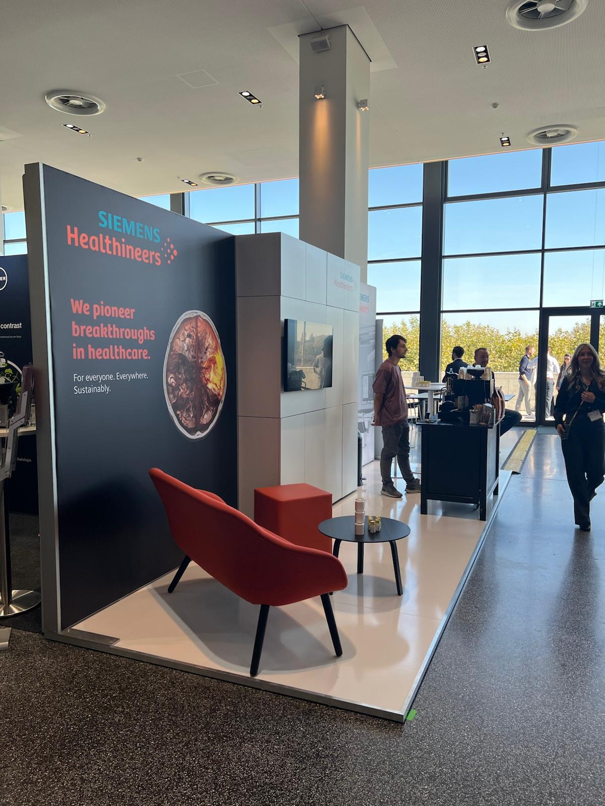 Siemens Healthineers exhibition booth with dark display panel, red seating, and healthcare imagery in modern office setting