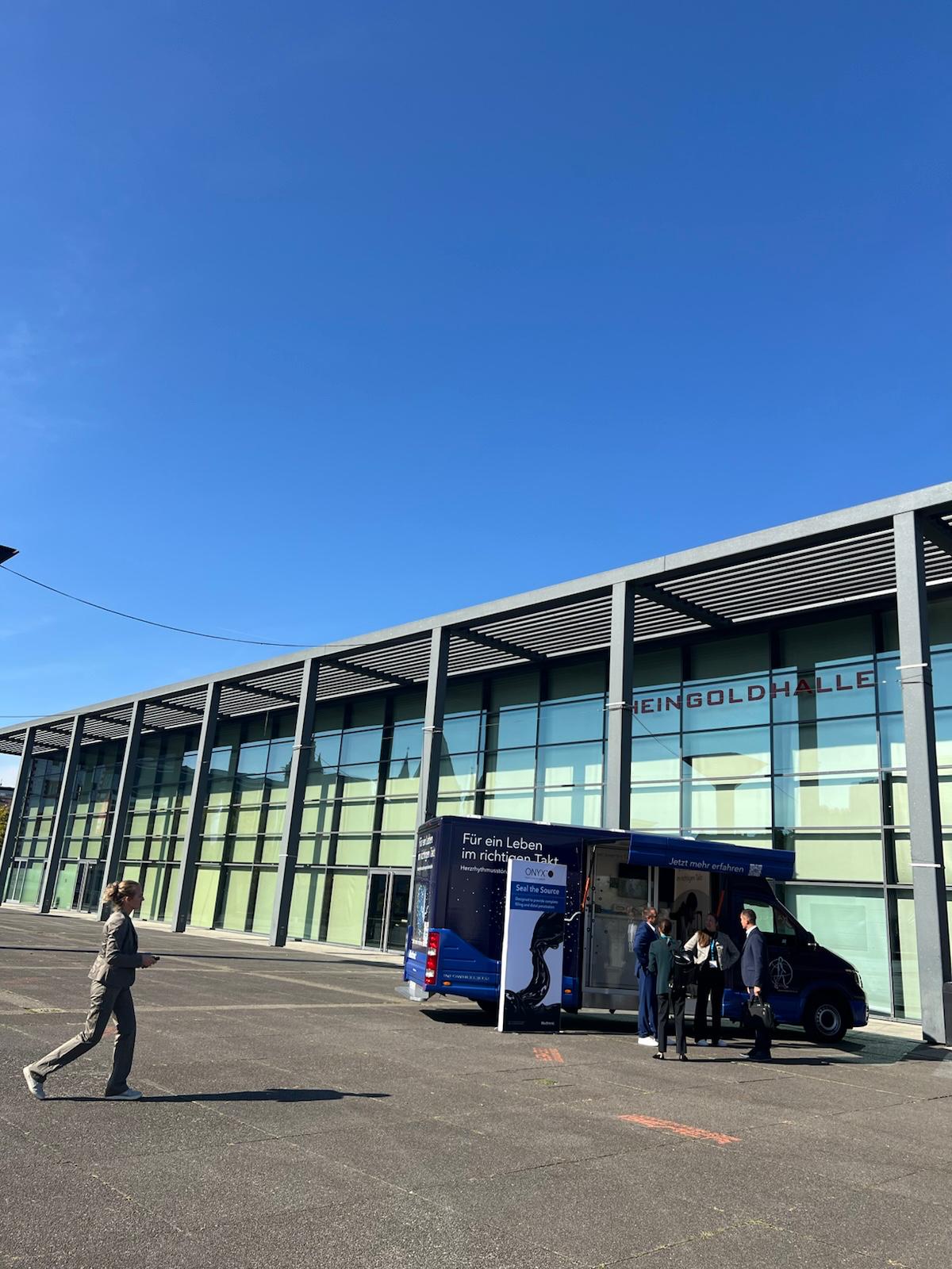 Modern glass building facade with metal framework and parked blue information vehicle under clear blue sky