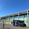 Modern glass building facade with metal framework and parked blue information vehicle under clear blue sky