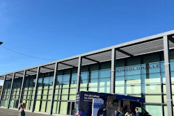 Modern glass building facade with metal framework and parked blue information vehicle under clear blue sky
