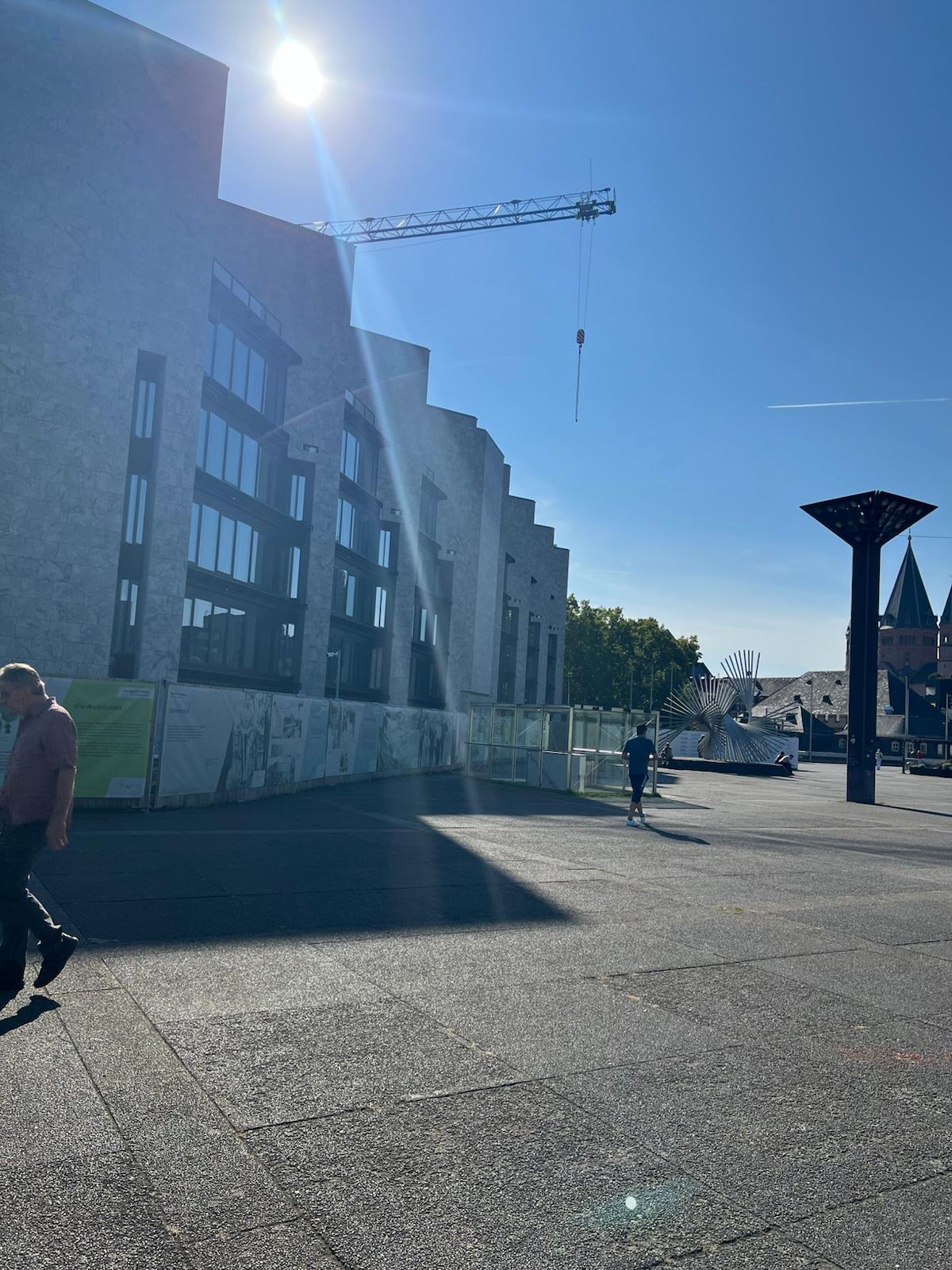 Construction site with modern building facade, crane, and sculptural public art installation under clear blue sky
