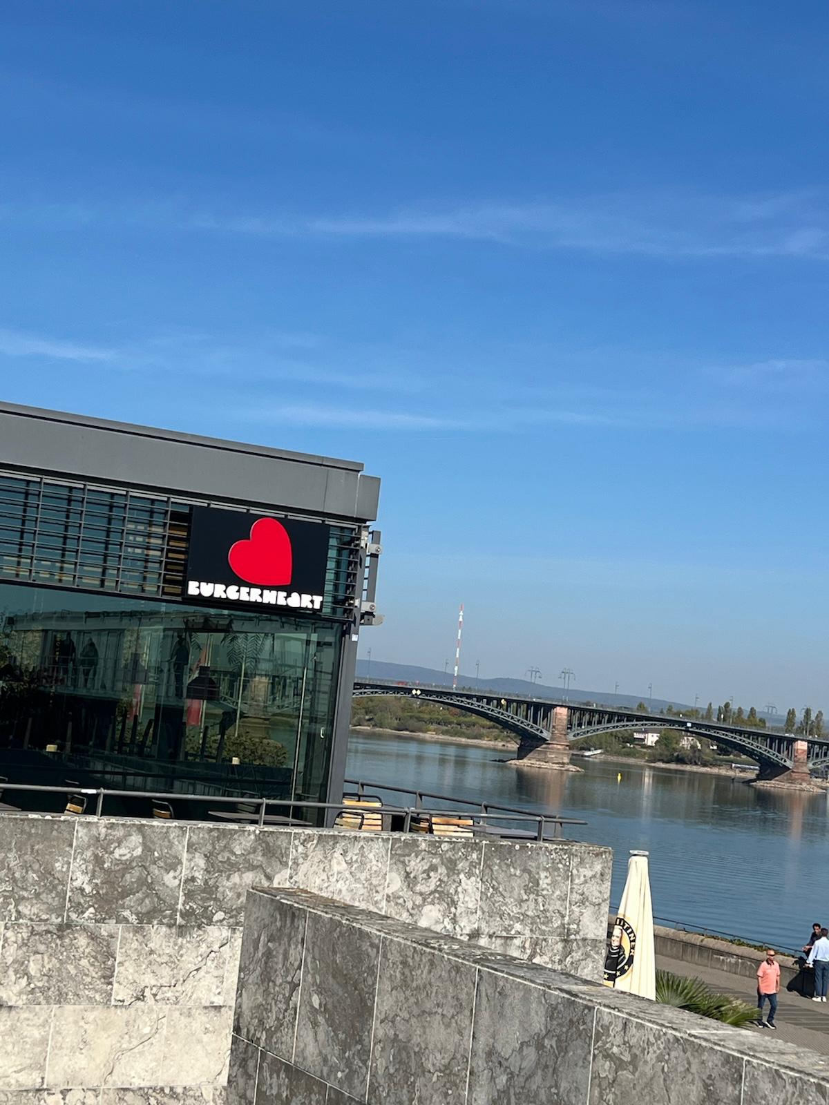 BurgerHeart restaurant storefront with red heart logo overlooking a river and bridge on a clear day