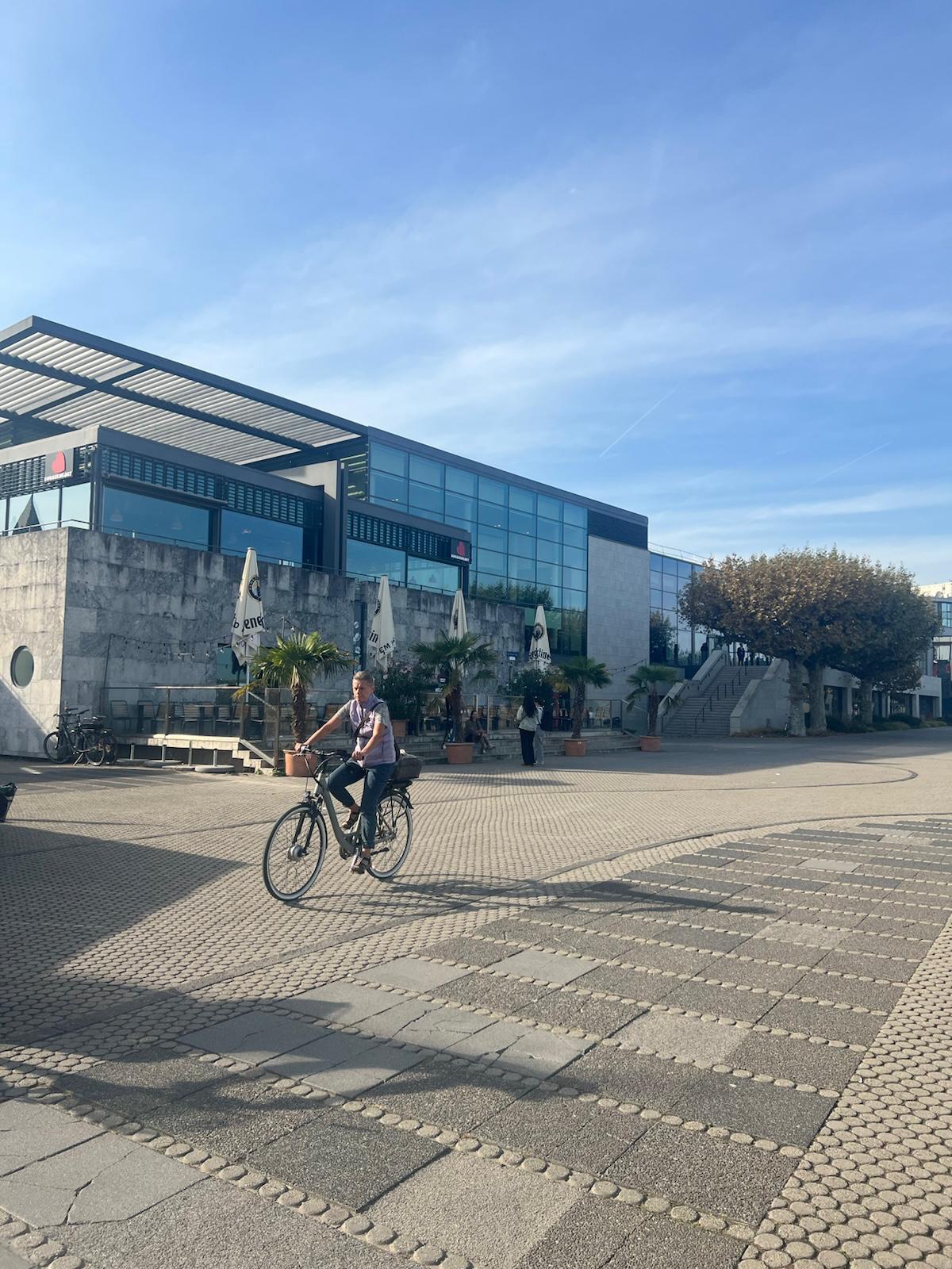 Cyclist riding through modern plaza in front of contemporary glass and concrete building on sunny day