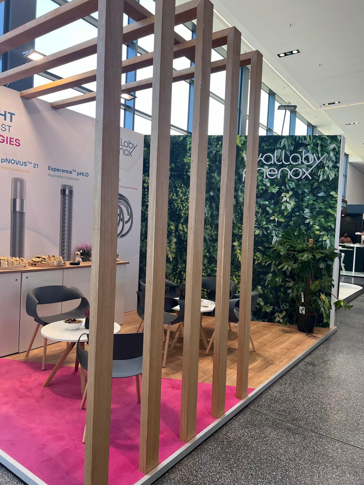 Modern exhibition booth with wooden lattice frame, pink carpet, living green wall backdrop, and Callaby Genox branding signage