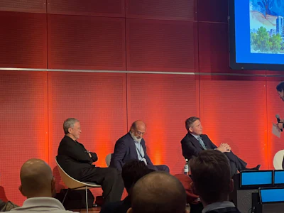 Three business professionals participate in a panel discussion on stage with red lighting backdrop