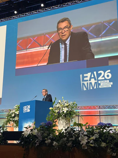 Speaker presenting at EA NM 26 World Leading Meeting conference podium with floral arrangements