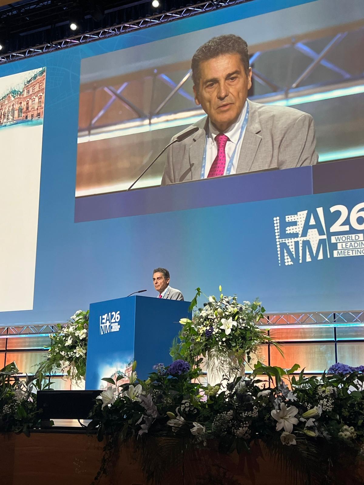 Speaker presenting at EIA26 NVM World Leading Meeting conference with podium and large screen display
