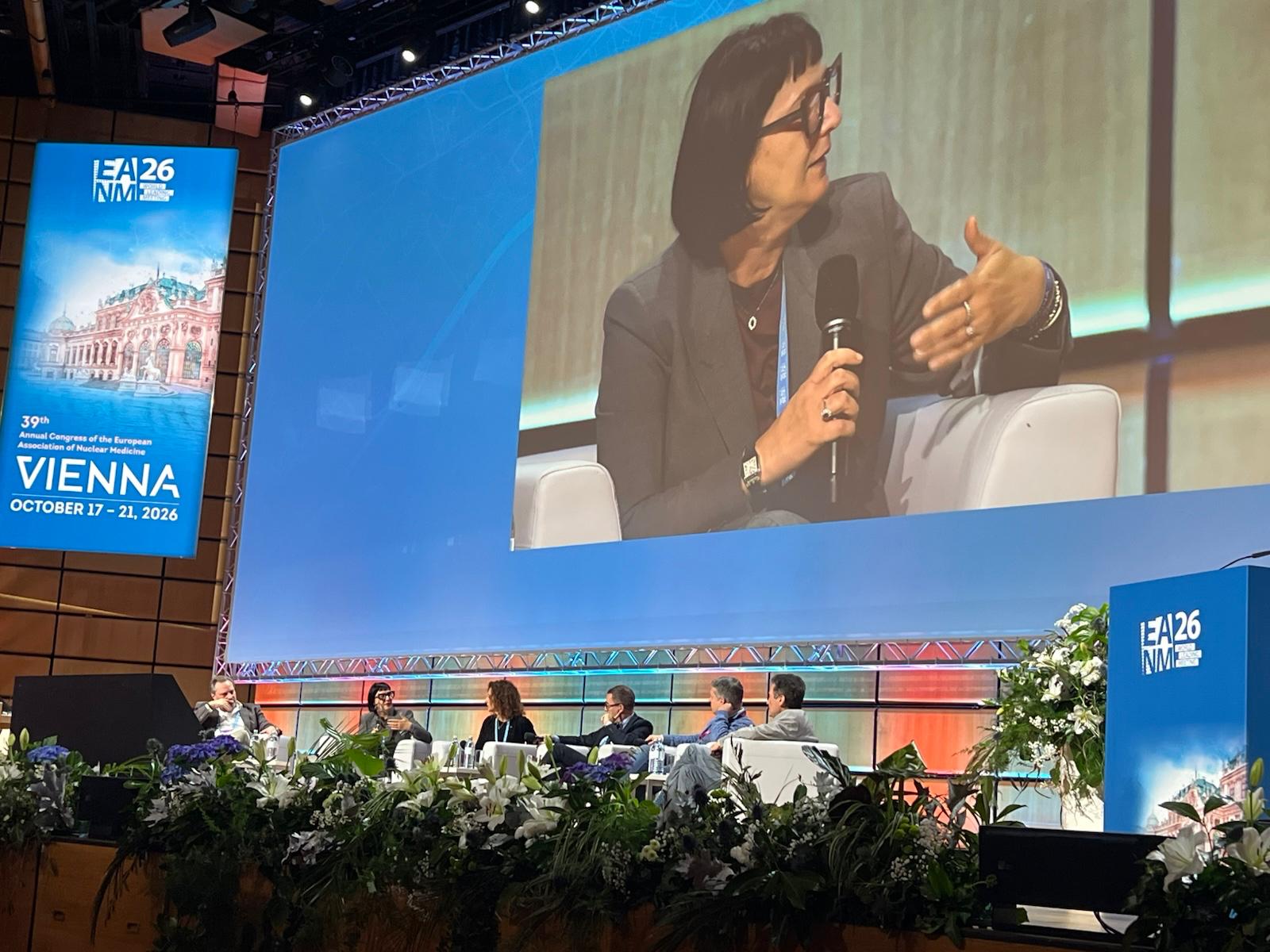 Panel discussion at ISTAT26 conference in Vienna with speaker presenting on stage while seated panelists listen