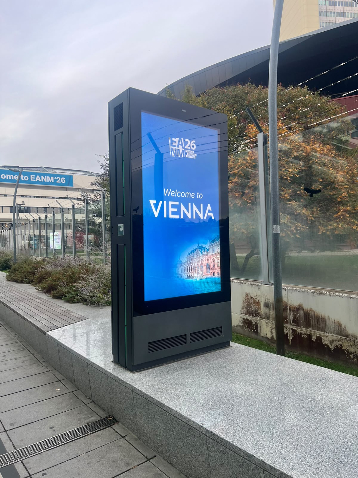 Digital outdoor display screen showing 'Welcome to VIENNA' with architectural imagery and EANM'26 branding in an urban plaza setting