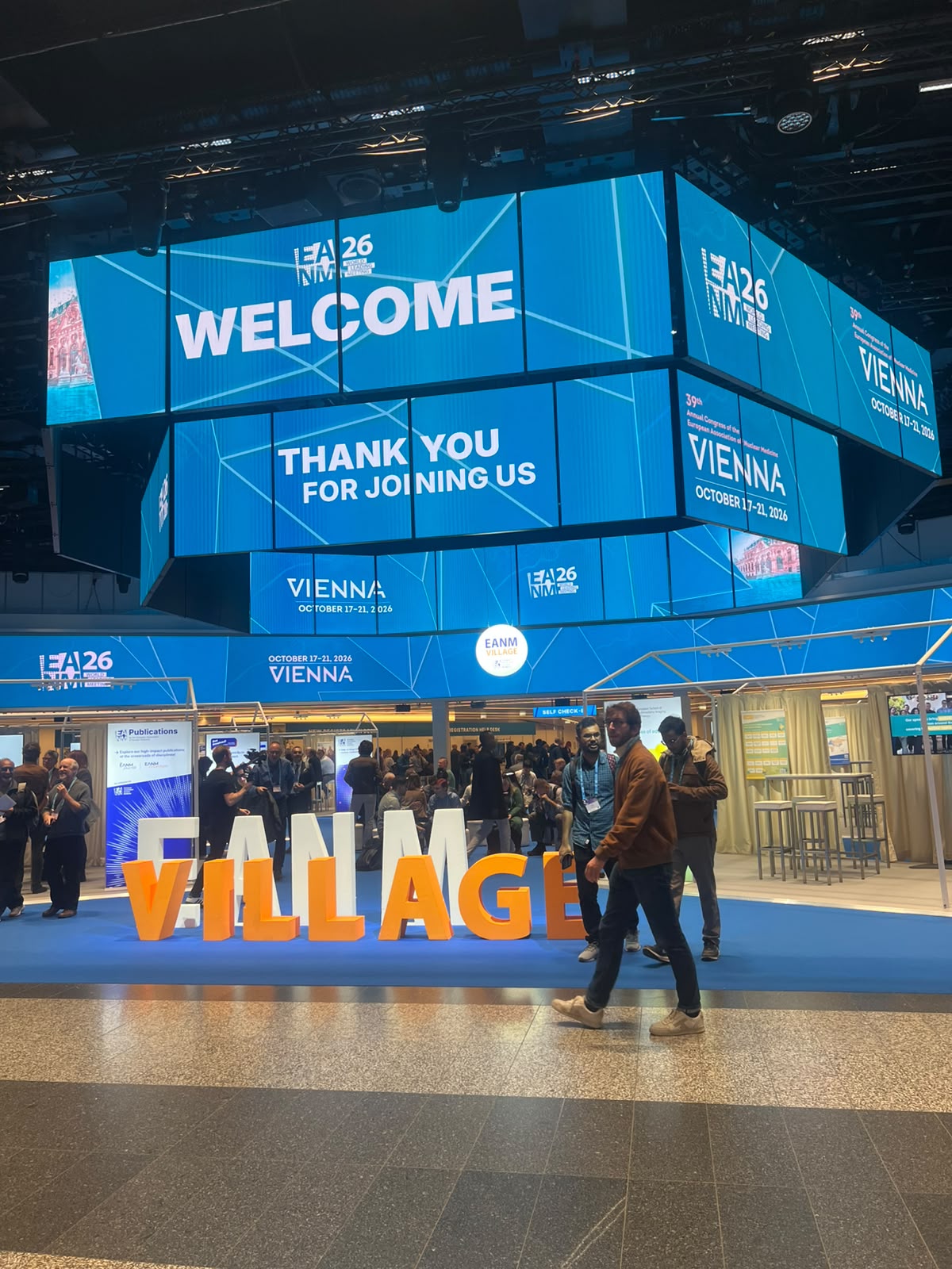 EIA26 Vienna conference venue with blue overhead displays welcoming attendees and orange 'VILLAGE' signage at the entrance