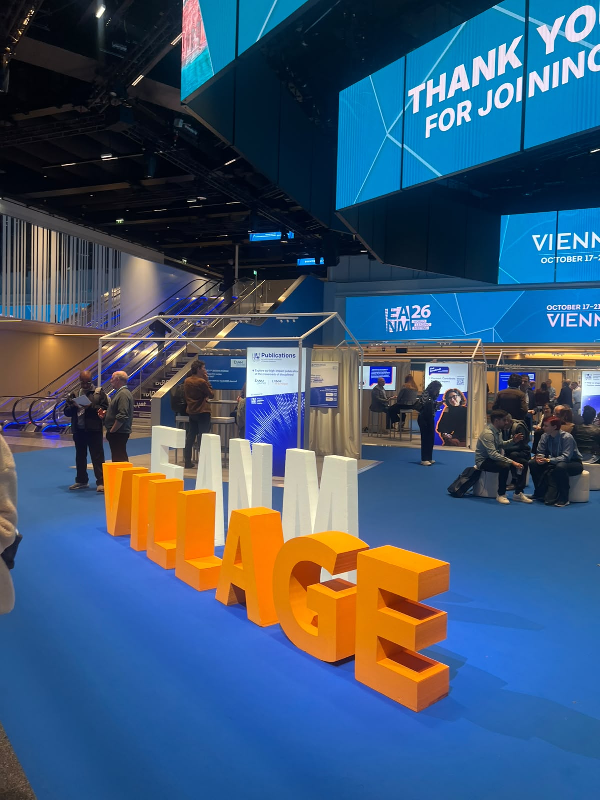 Large orange and white 3D letter installation at IEA26 Vienna conference venue with blue flooring and exhibition booths