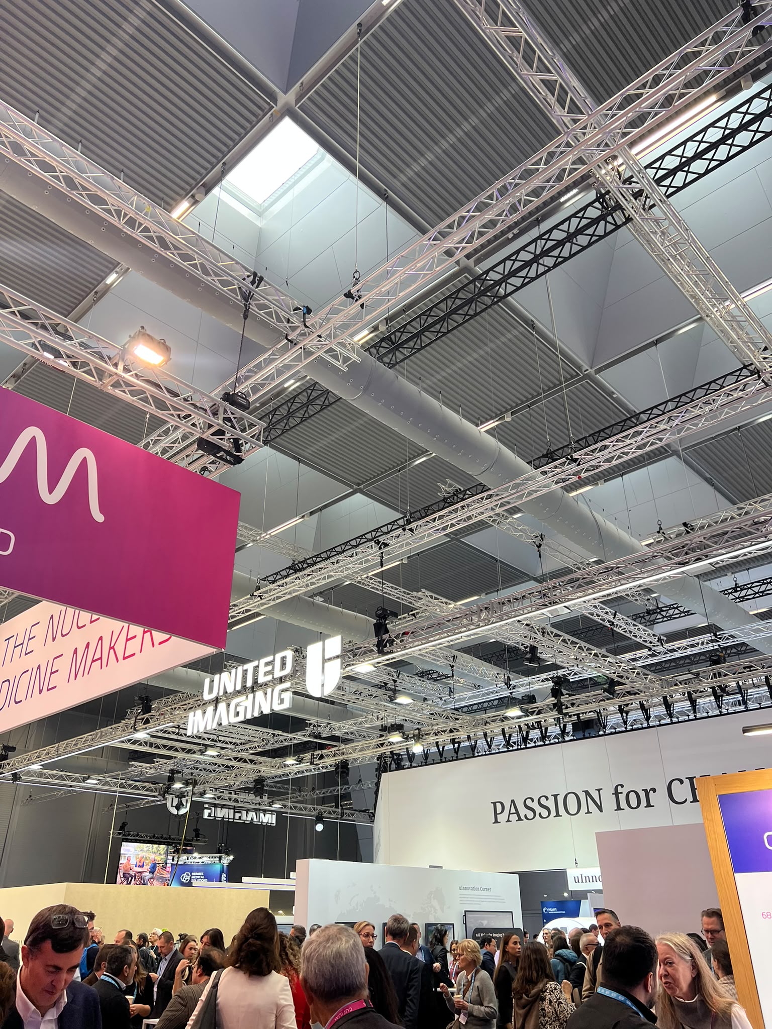Crowded exhibition hall with industrial ceiling, metal trusses, and branded signage including United Marketing booth